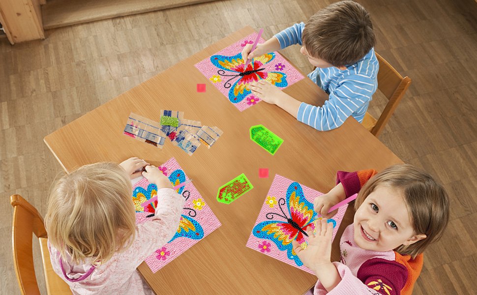Three children doing diamond art kits with butterfly designs on a wooden table, with gems and tools scattered around.