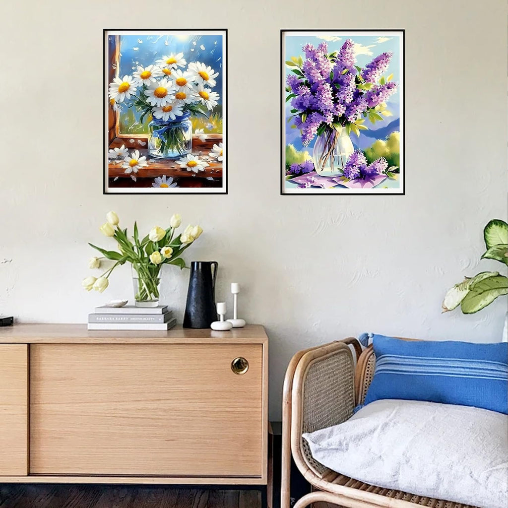 Two framed diamond paintings of floral arrangements hanging on a wall above a wooden cabinet.