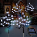 Three snowflake stake lights with a solar panel in a snowy yard at dusk