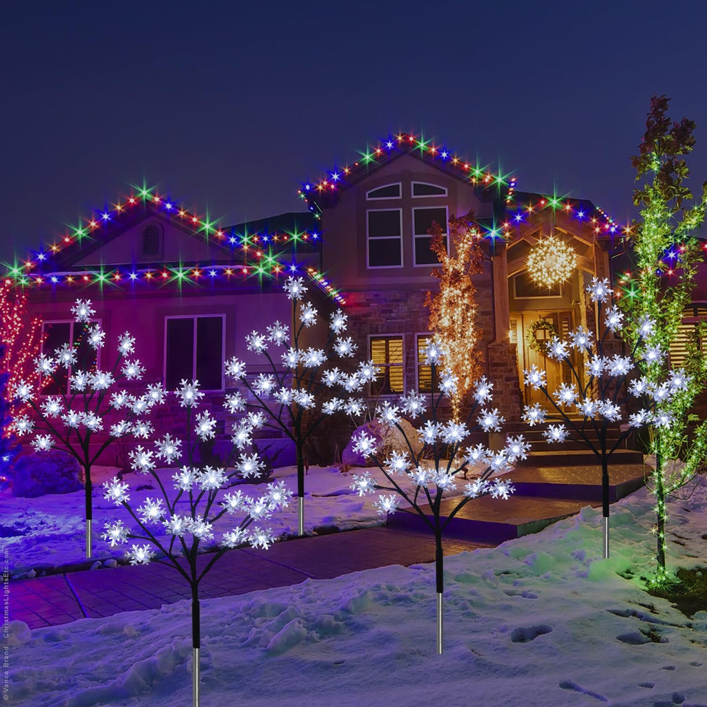 Snowflake stake lights and colorful roofline lights decorate a house exterior at night