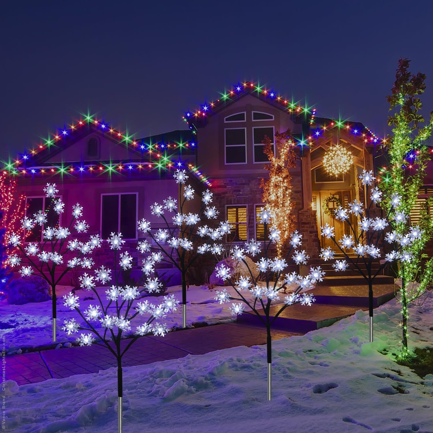 Snowflake stake lights and colorful roofline lights decorate a house exterior at night