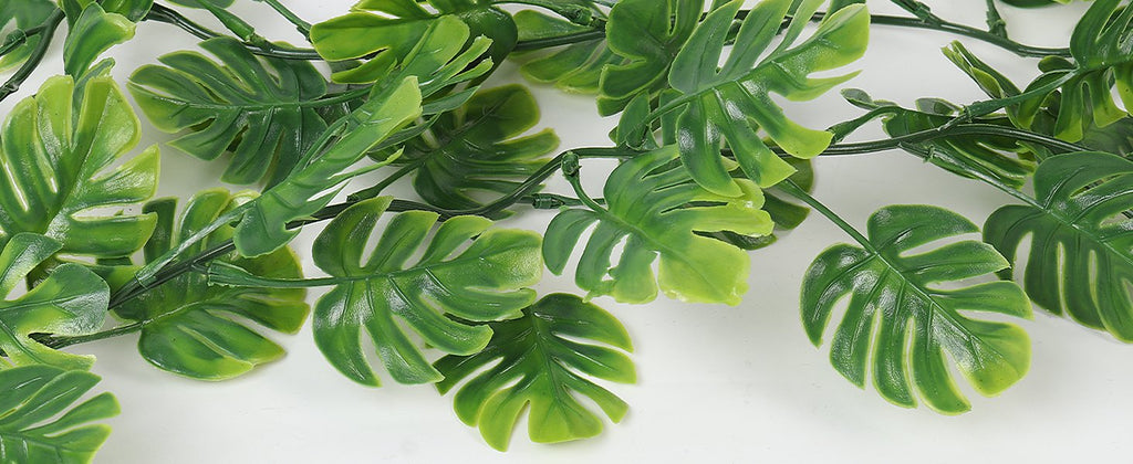 Close-up of artificial monstera leaves and vines on a white background.