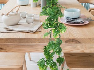 Artificial monstera vine draped across a wooden dining table with place settings