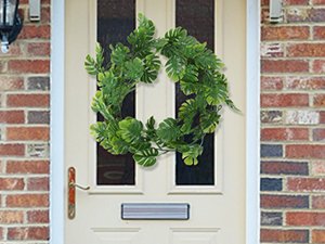 Artificial monstera wreath hanging on a cream-colored front door with brick surround