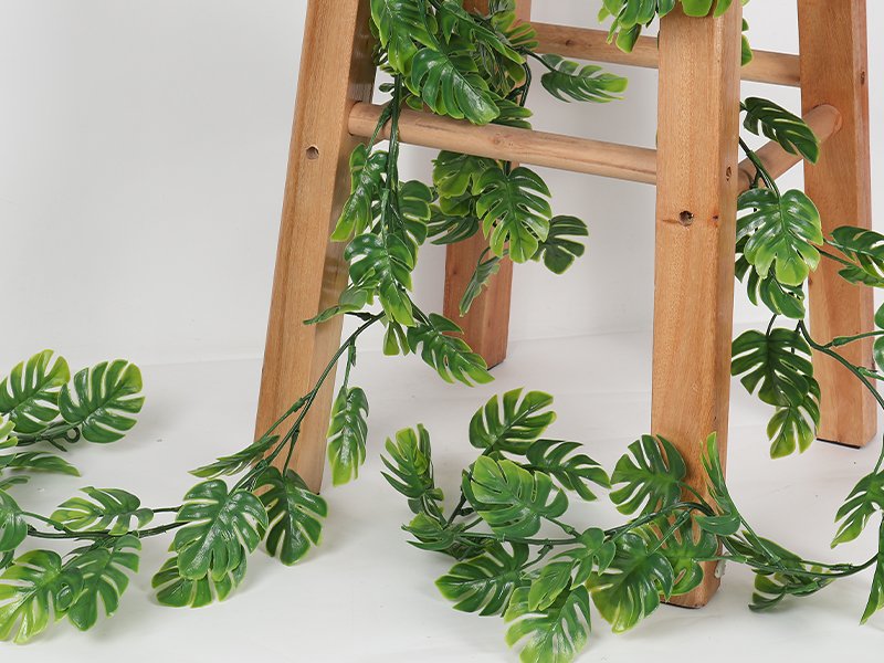 Artificial monstera vines draped over a wooden stool, showcasing realistic green leaves and stems.