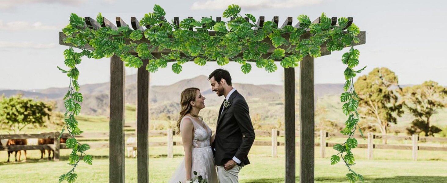 Wedding couple standing under a wooden arbor decorated with artificial monstera vines