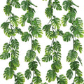 Four artificial monstera vines with green leaves cascading against a white background.