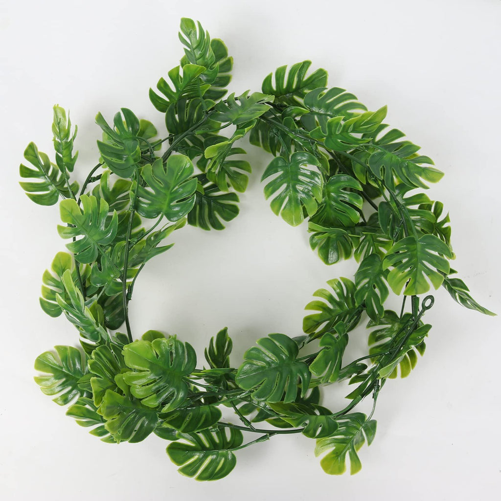 Artificial monstera vine garland with large green leaves arranged in a circular shape on a white background.