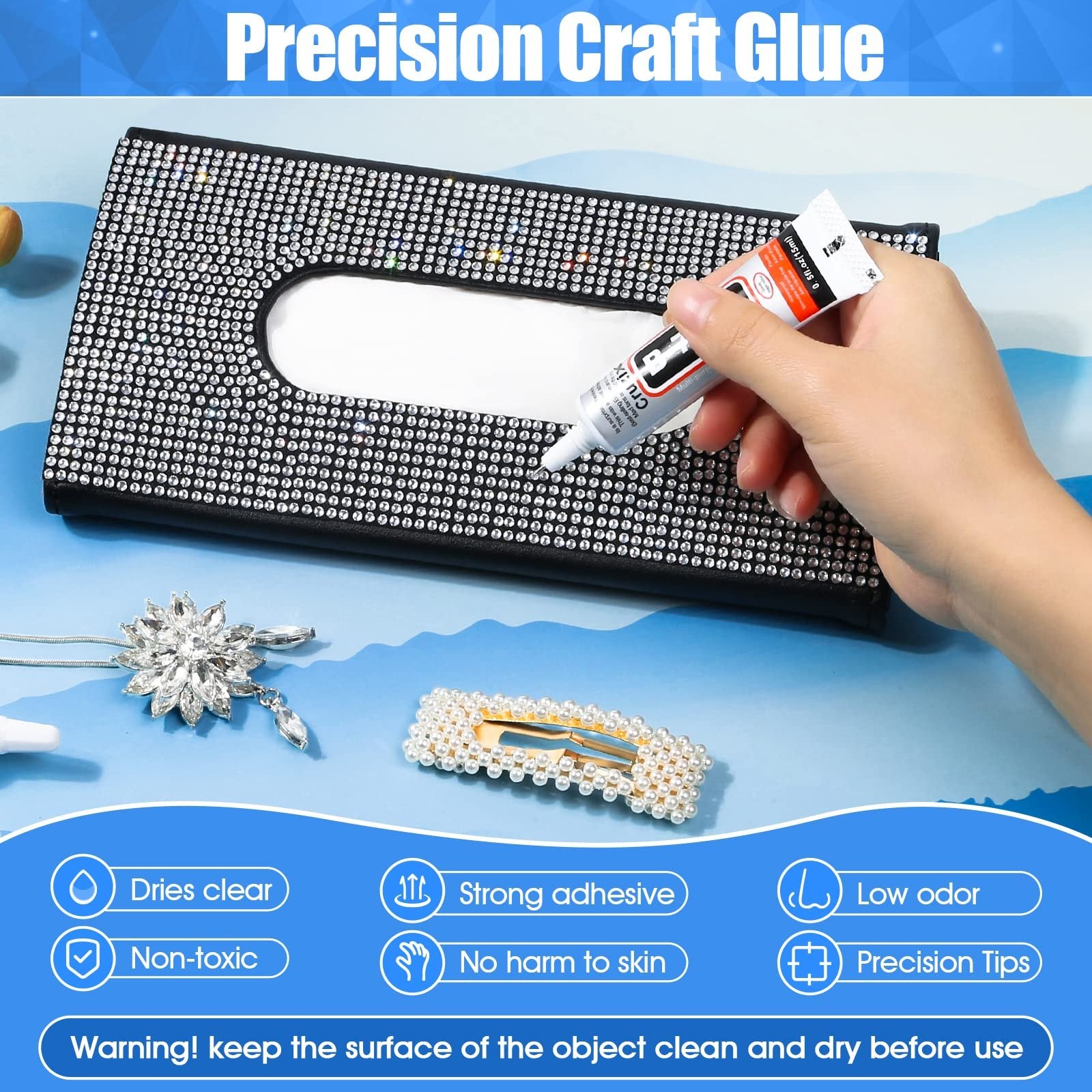 Hand holding a tube of clear adhesive glue, applying it to a rhinestone-covered tissue box, with craft supplies nearby.
