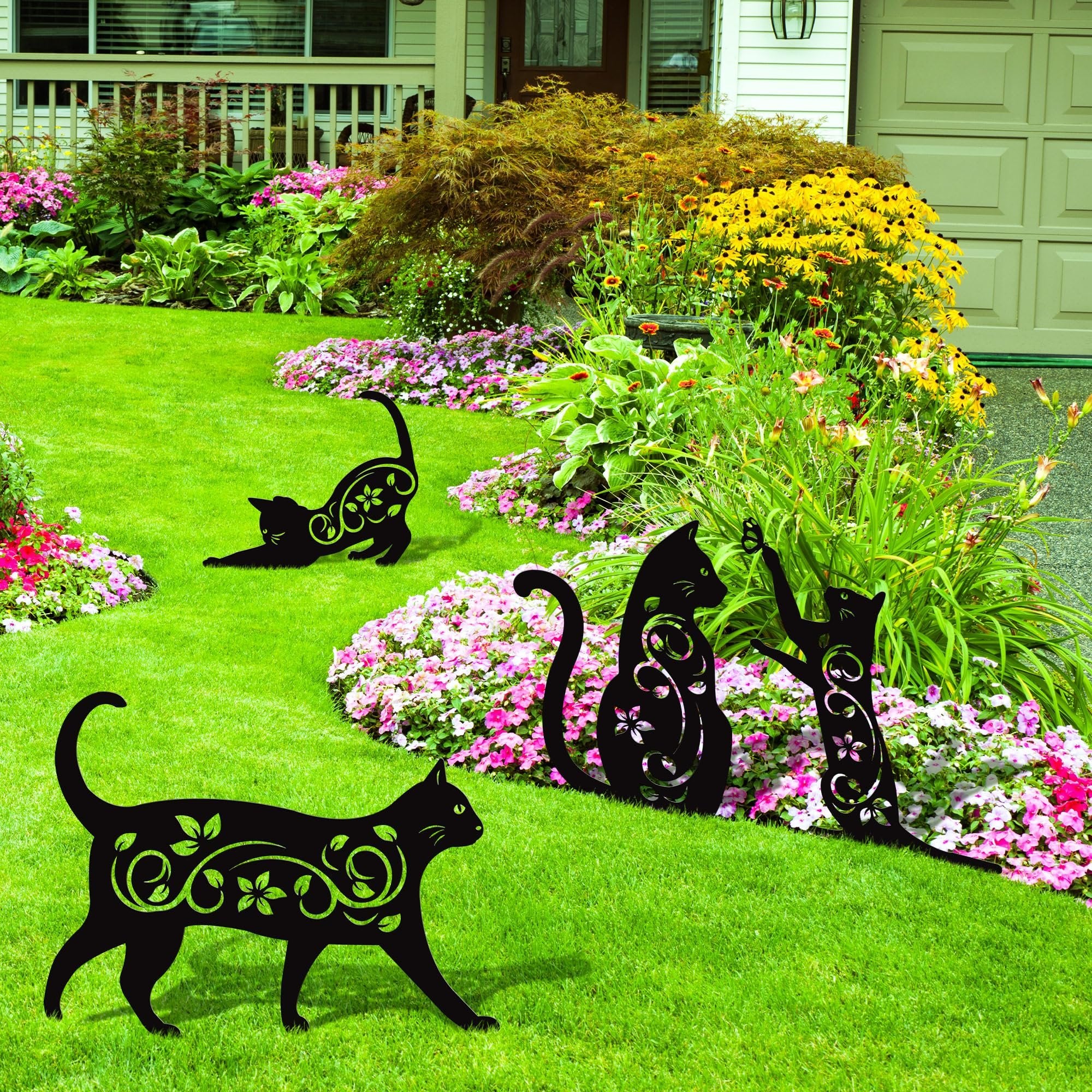 Four black metal cat silhouettes with floral cutouts placed in a lush garden with pink and yellow flowers.