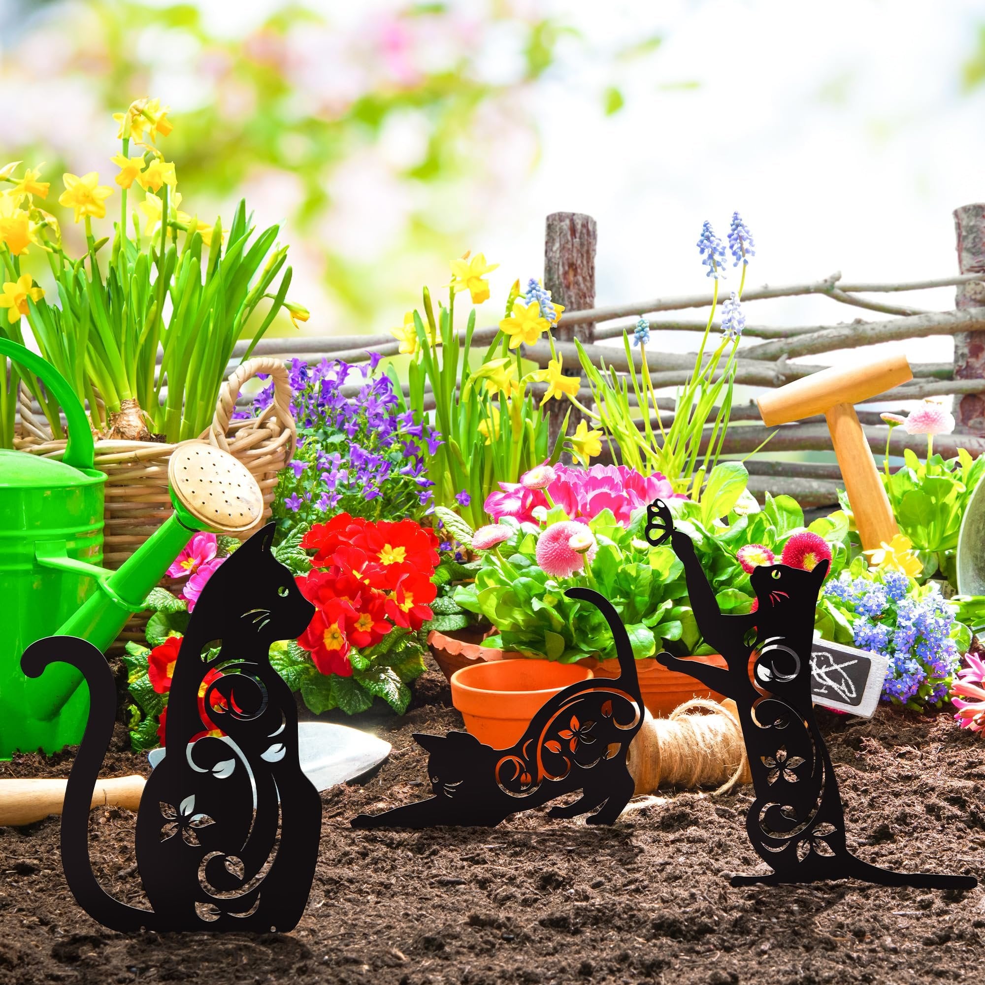 Four black metal cat silhouette garden stakes with floral cutouts placed in soil with spring flowers and gardening tools.