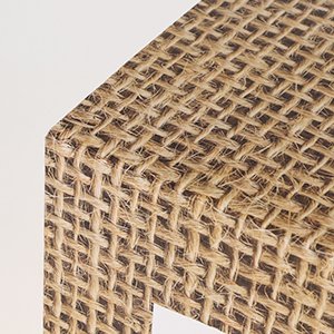 Close-up of a rustic burlap-print baby box corner, showing woven texture and white edge.