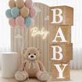 Four burlap baby blocks spelling BABY, a teddy bear, and pastel balloons for a baby shower decoration setup.