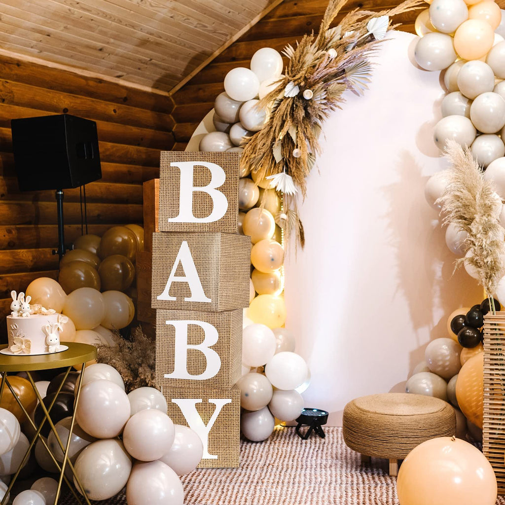 Four burlap baby blocks spelling 'BABY' stacked vertically, part of a festive baby shower decoration with balloons and a cake.