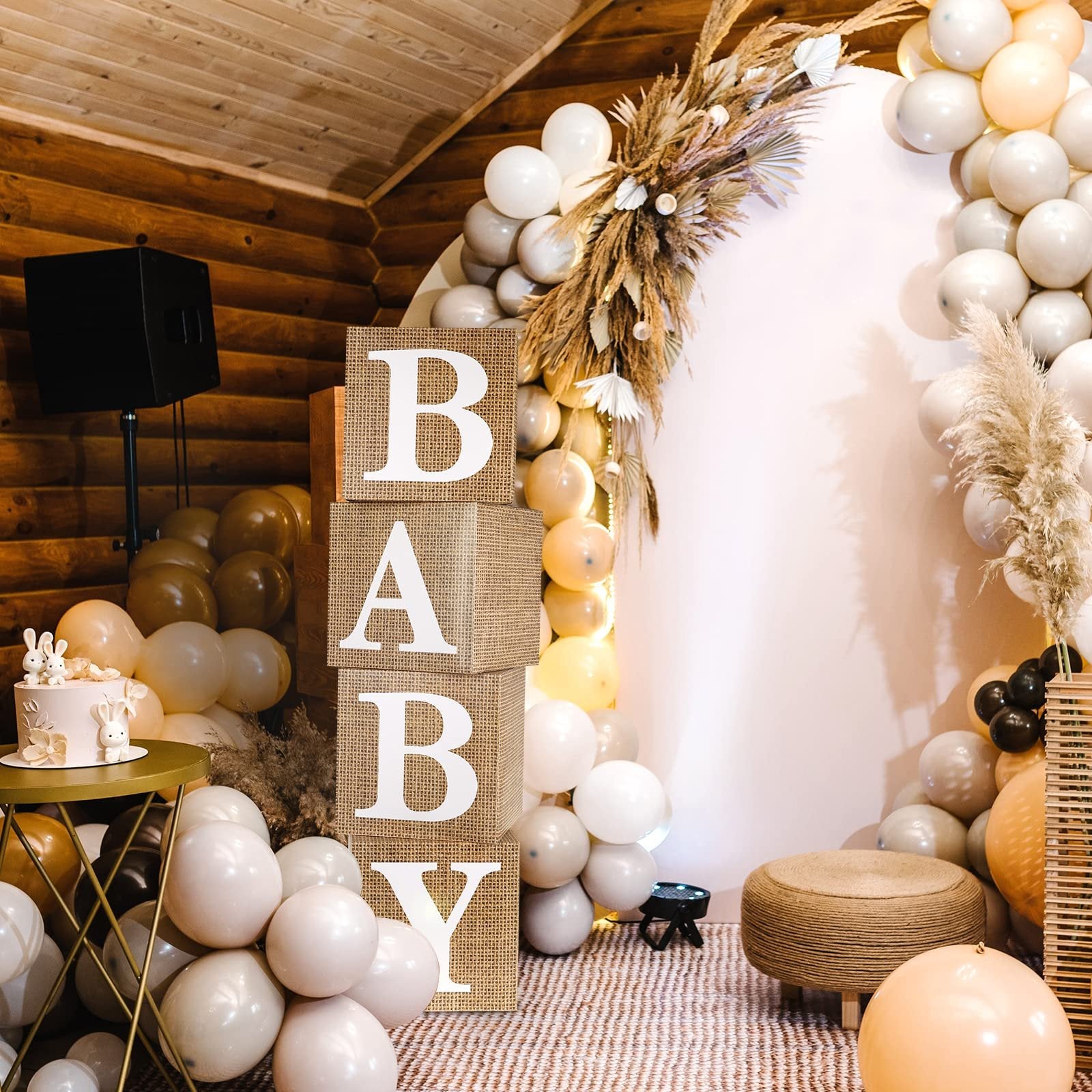 Four burlap baby blocks spelling 'BABY' stacked vertically, part of a festive baby shower decoration with balloons and a cake.