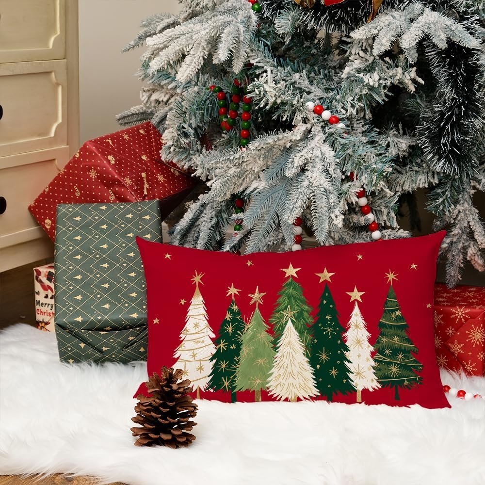 Red lumbar pillow cover with Christmas trees and gold stars, set by a flocked Christmas tree and gifts.