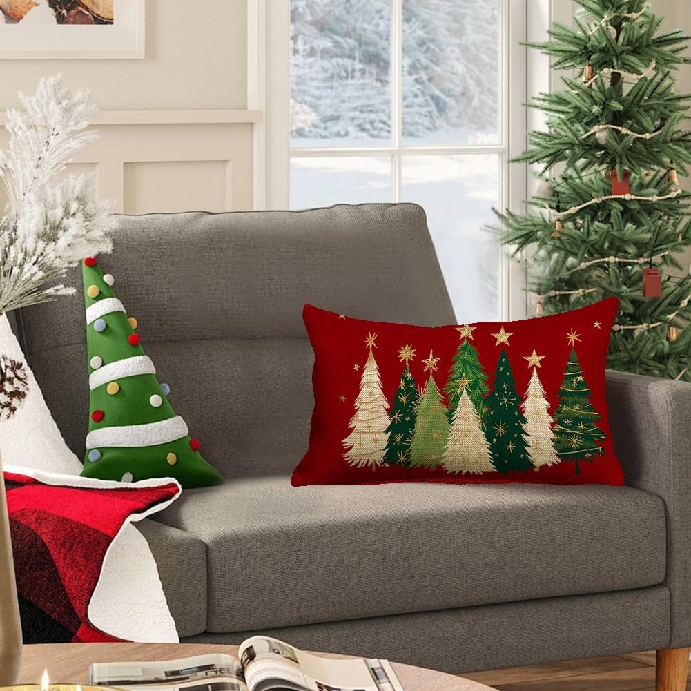 Red lumbar pillow cover with gold and green Christmas trees and stars, on a gray sofa next to a Christmas tree.