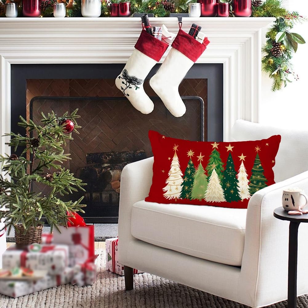 Christmas pillow cover with red background and green and white trees with gold stars, on a white armchair by a fireplace.