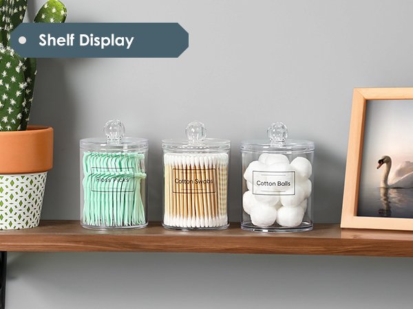 Clear acrylic bathroom canisters filled with cotton swabs, cotton balls, and floss picks on a shelf.