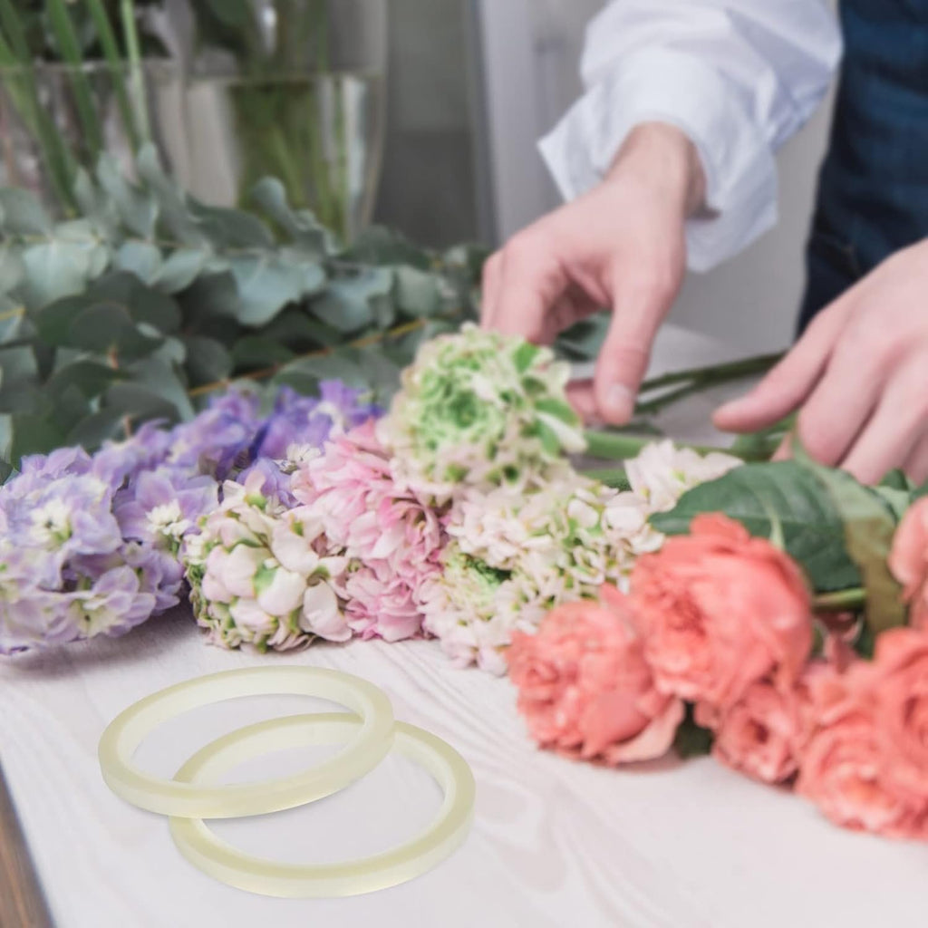Two clear floral tape rolls on a wooden surface with a florist arranging flowers in the background.