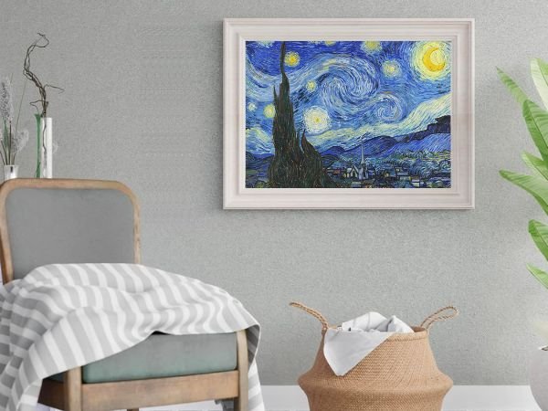 Framed Van Gogh Starry Night painting hanging on a textured gray wall above a chair with a striped blanket and a woven basket.