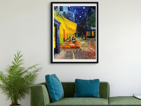 Framed diamond painting of Van Gogh's Cafe Terrace at Night hanging on a wall above a green sofa.