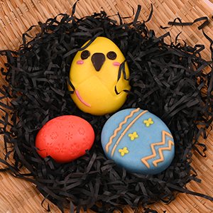 Easter chocolate molds shaped like a chick, egg, and half egg, nestled in black shredded paper within a basket.