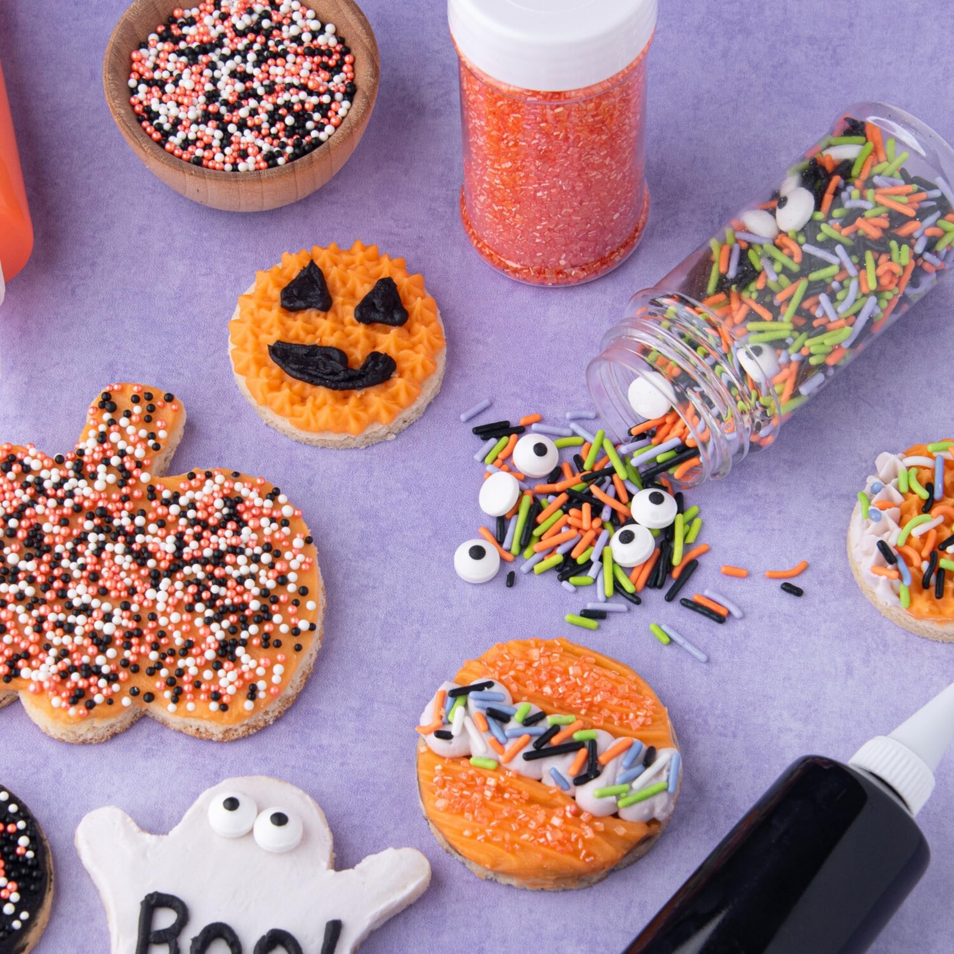 Halloween-themed decorated cookies with various sprinkles and black icing tube on a purple background