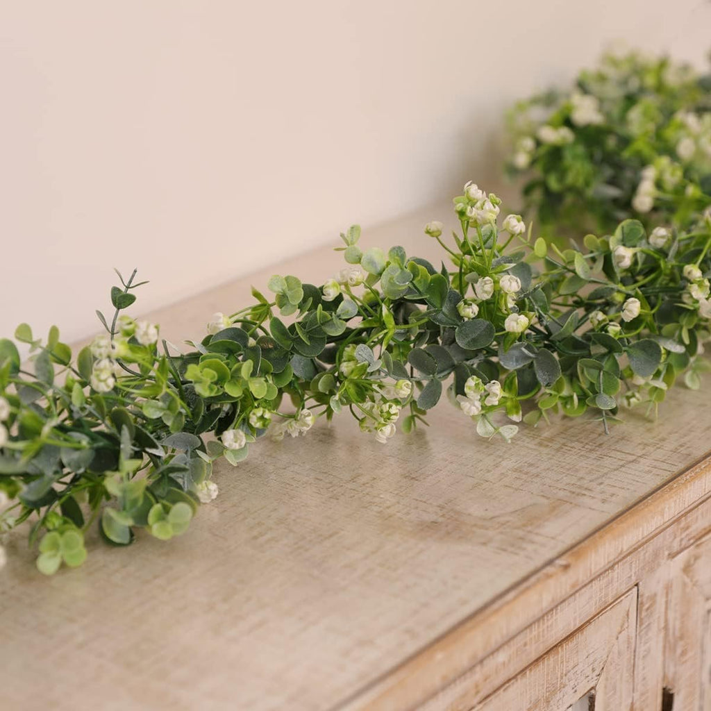 Faux eucalyptus garland with white flowers draped on a wooden surface