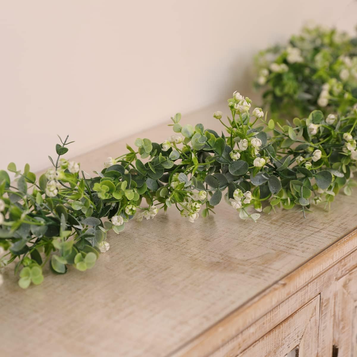Faux eucalyptus garland with white flowers draped on a wooden surface