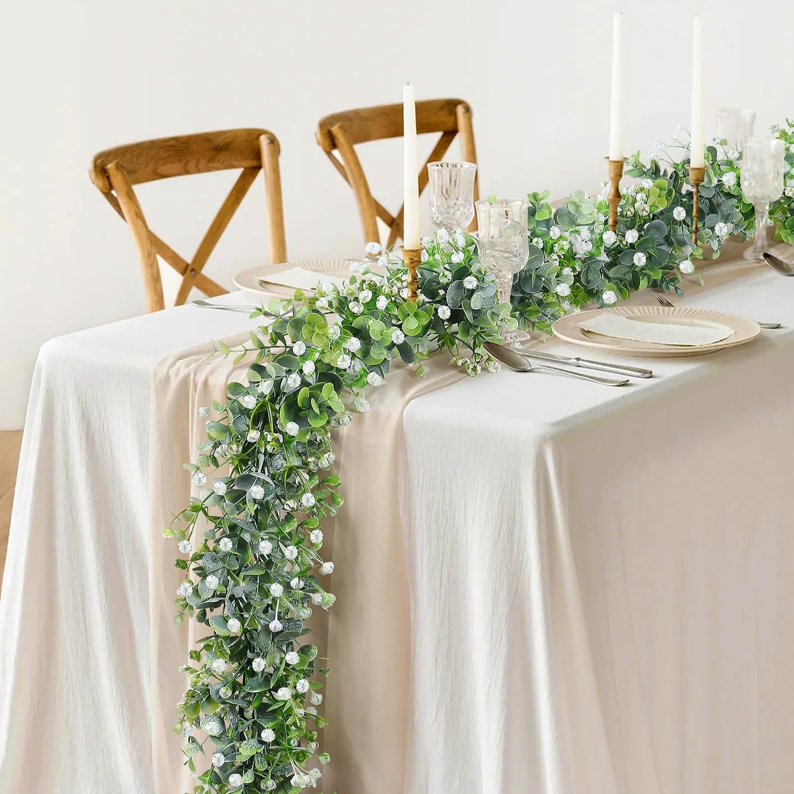 Faux eucalyptus garland with white flowers draped across a table setting with candles and chairs
