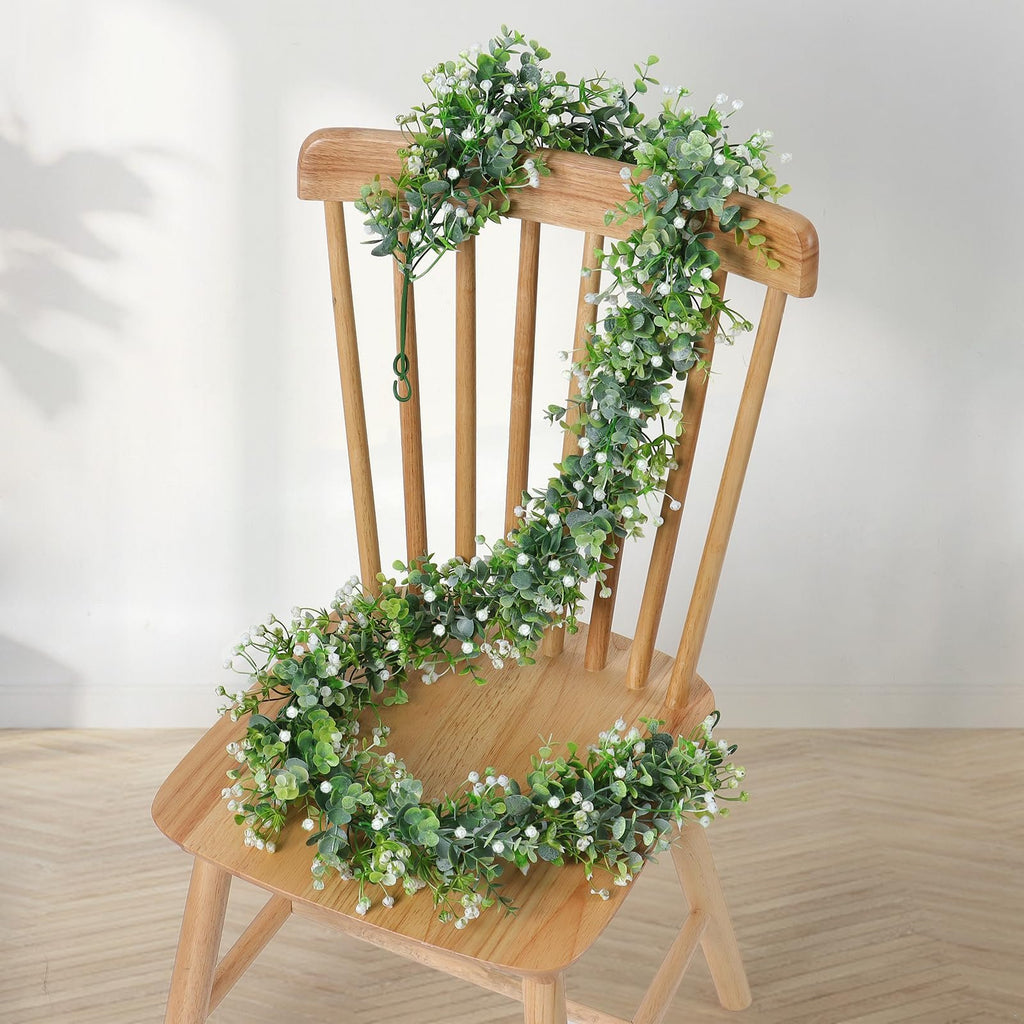 Faux eucalyptus garland with white flowers draped over a wooden chair