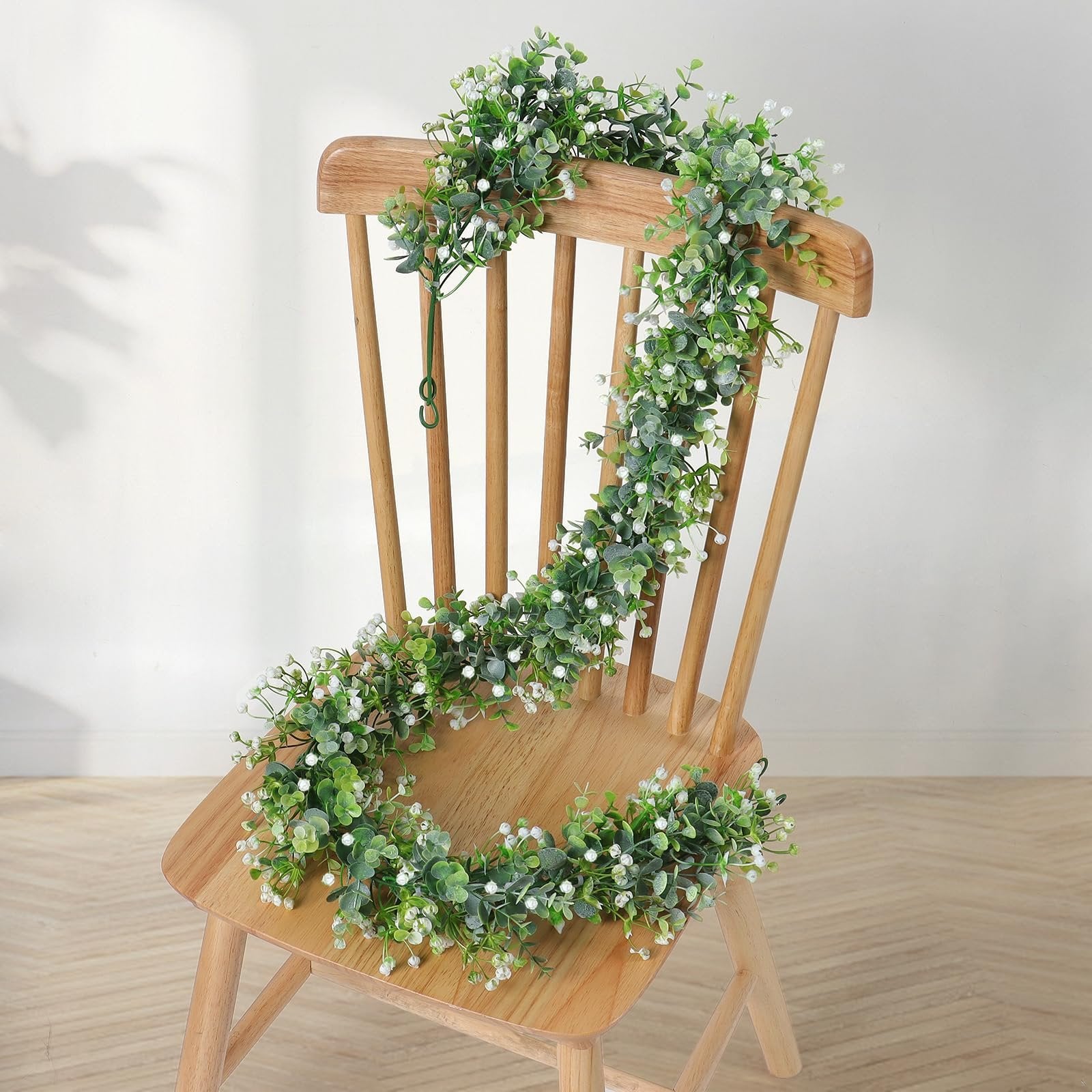 Faux eucalyptus garland with white flowers draped over a wooden chair