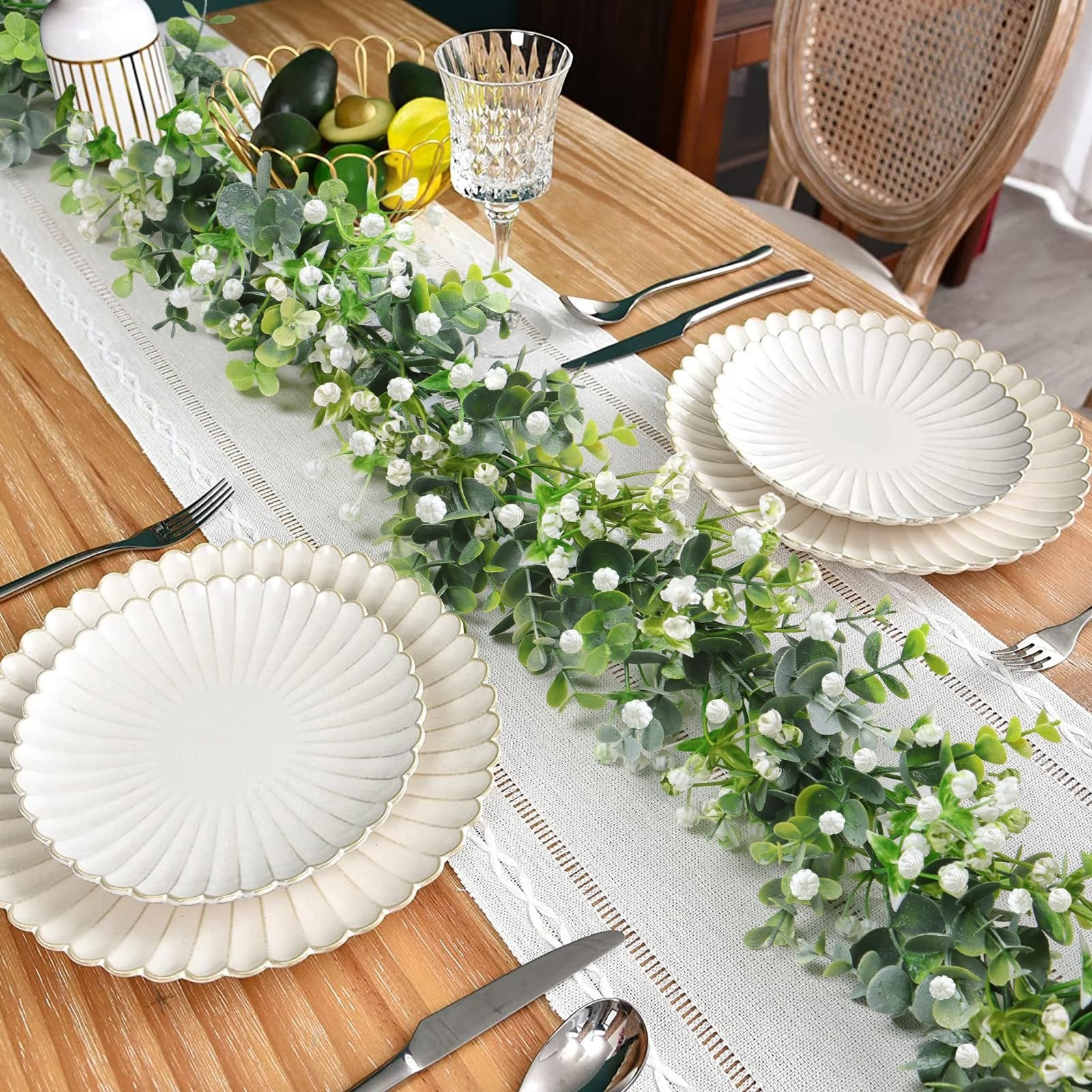 Faux eucalyptus garland with white flowers draped across a table setting with plates and cutlery.