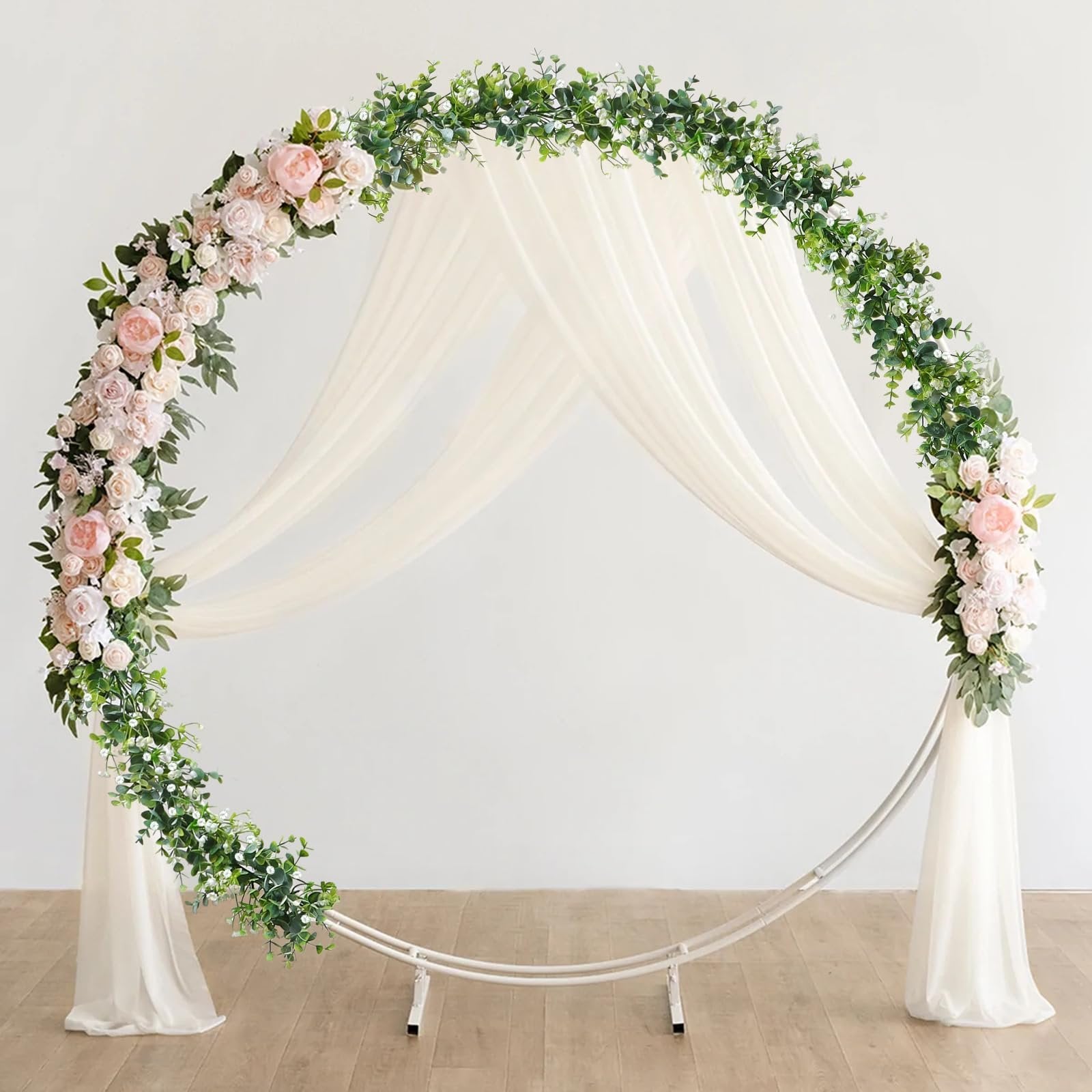 Circular wedding arch decorated with faux eucalyptus garland and pink roses, draped with sheer fabric.