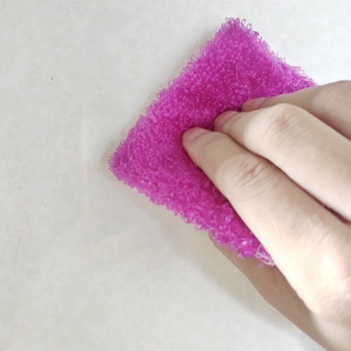 Hand holding a pink scrubbing pad against a textured white surface