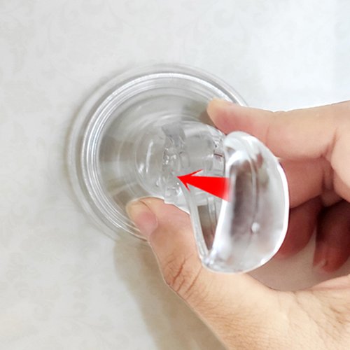 Close-up of a hand attaching a clear suction cup hook to a tiled surface, with a red arrow indicating movement.
