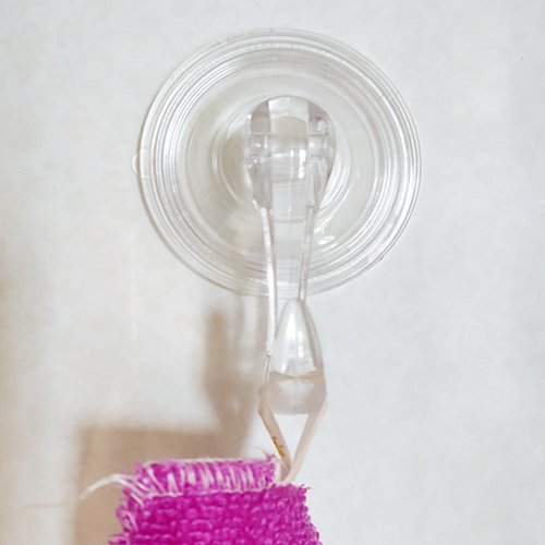 Clear polycarbonate suction cup hook holding a pink textured item against a tiled wall.