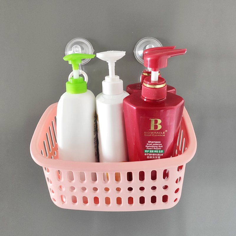 Pink plastic shower caddy with three pump bottles hanging on a wall with clear suction cups