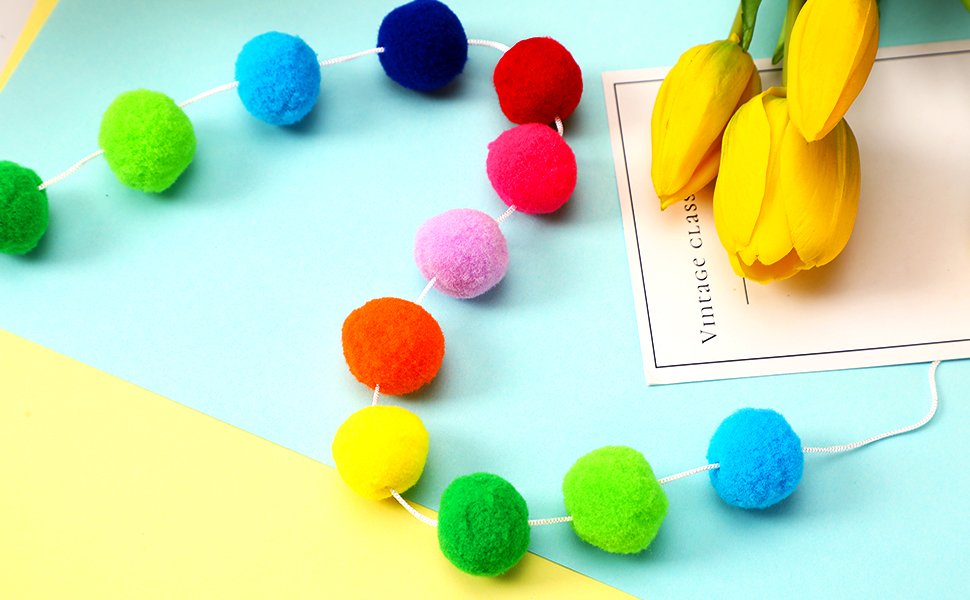 Rainbow pom pom garland with 30 balls each, displayed on a pastel blue and yellow background with yellow tulips.