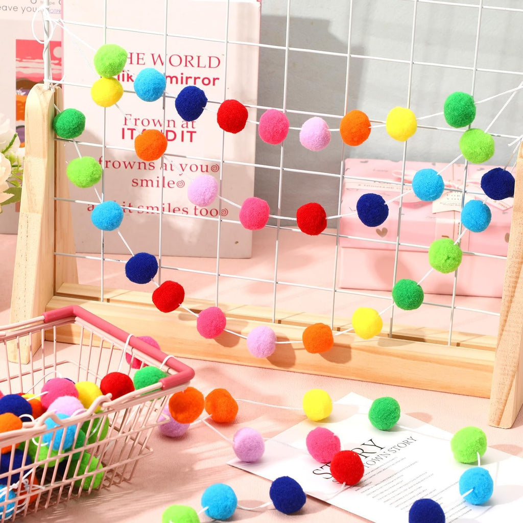 Rainbow pom pom garland strings with 30 balls each, displayed on a wire grid and in a basket.