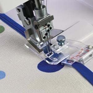 Sewing machine foot attaching blue bias tape to polka dot fabric with clear presser foot guide