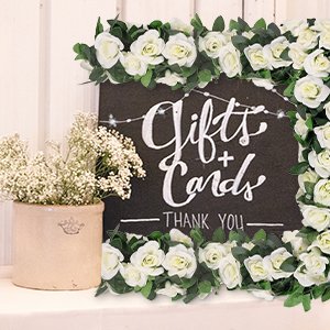 White artificial rose garlands with green leaves framing a 'Gifts + Cards THANK YOU' sign with fairy lights.