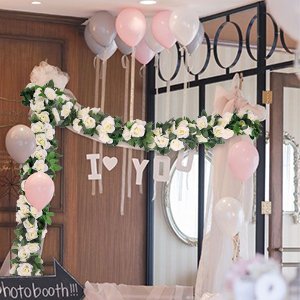 White artificial rose vine garlands with green leaves decorating a wedding arch with balloons and 'I LOVE YOU' sign