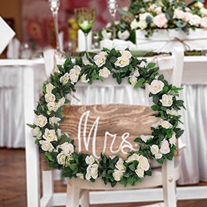 White artificial rose vine garland with green leaves arranged in a circle on a wooden sign that says Mrs.