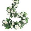 White artificial rose vine garland with green leaves, coiled on a white background.