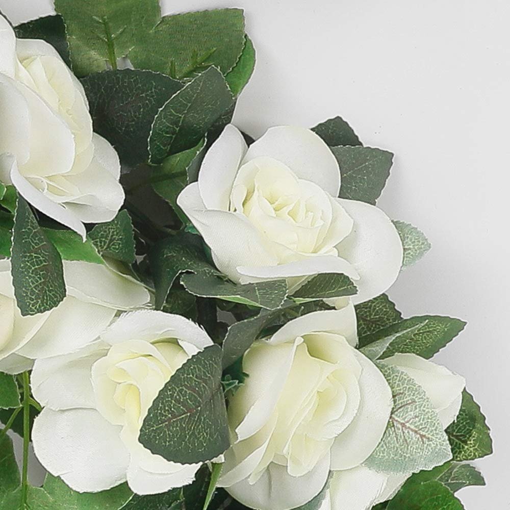 Close-up of white artificial rose garland with green leaves against a white background.