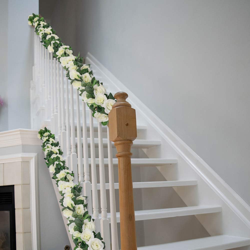 White artificial rose garlands with green leaves draped along a white staircase railing.