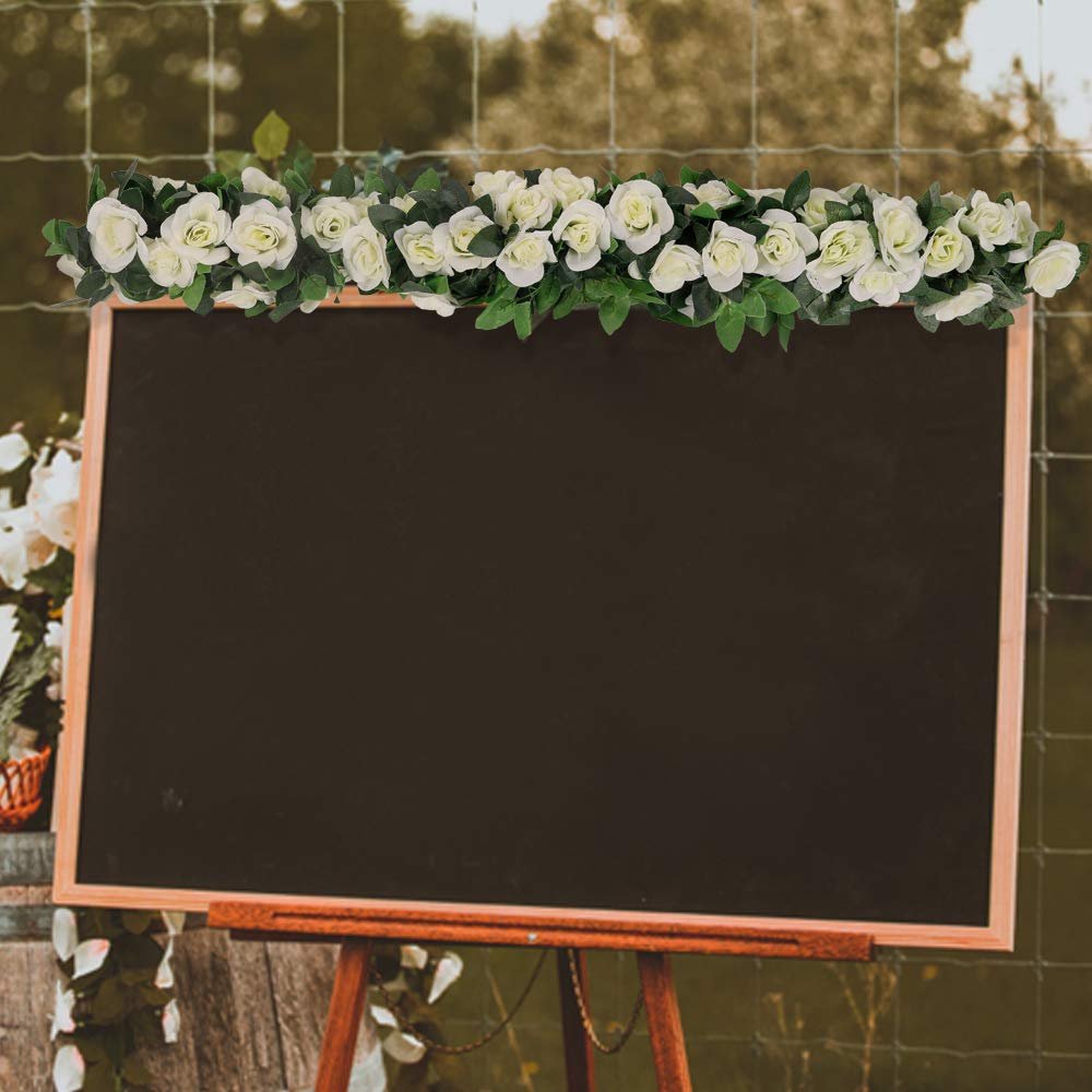 White artificial rose garland with green leaves draped across the top of a dark chalkboard on a wooden easel.