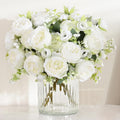 White silk peonies bouquet in a clear ribbed glass vase on a white surface, with soft lighting.